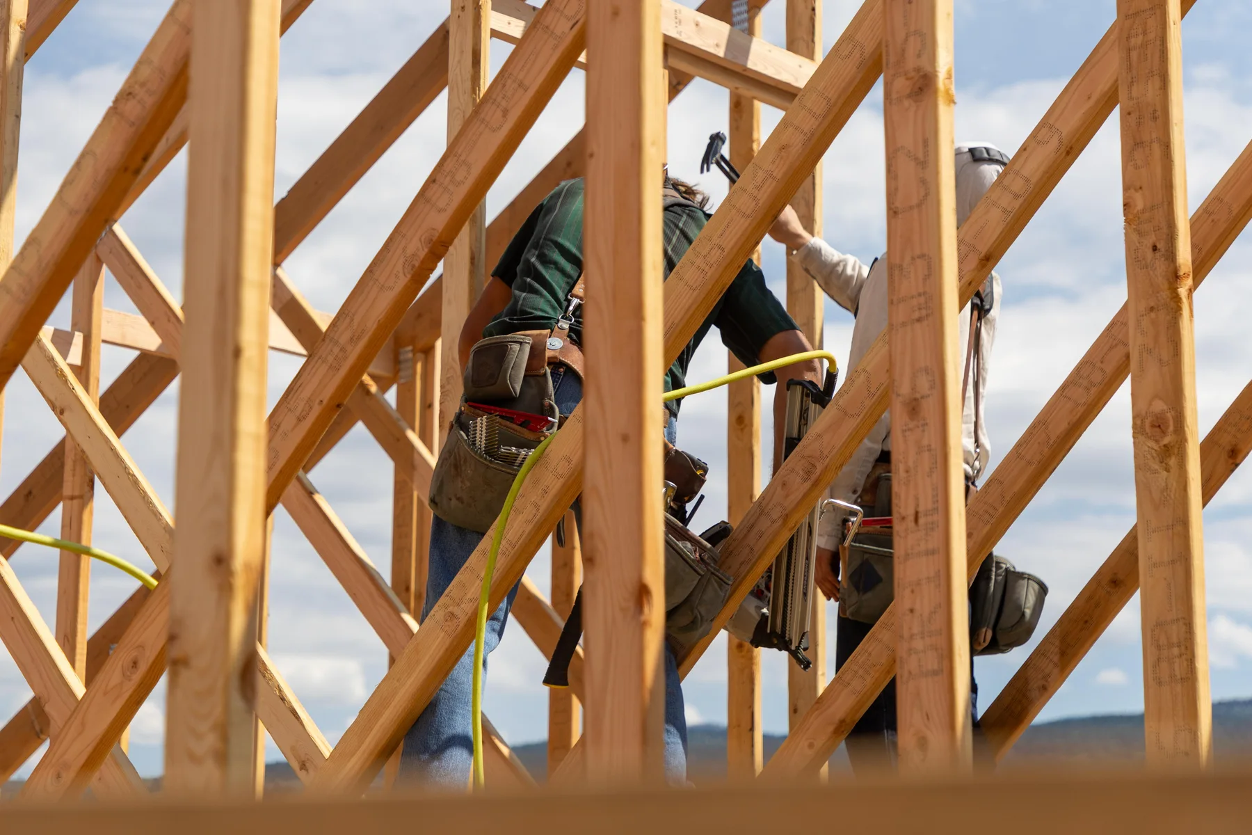 Two framers with tool belts working together between timber studs and braces